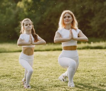 A mother and daughter practicing yoga together in matching outfits in a sunny park.