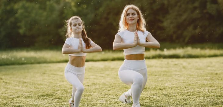 A mother and daughter practicing yoga together in matching outfits in a sunny park.
